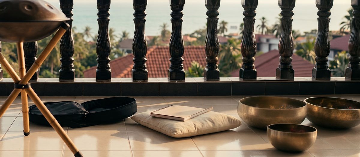 Singing bowls, a cushion and a handpan set out on the Noom terrace in Lamai, Koh Samui, with the sea behind